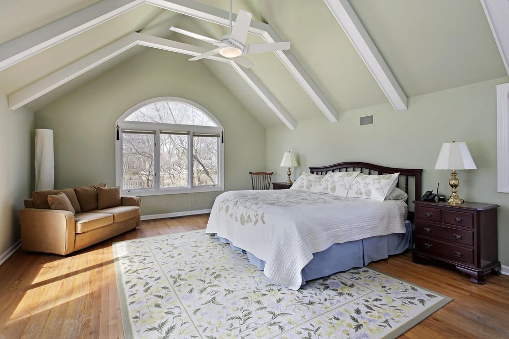 Traditional bedroom featuring a vaulted ceiling with beams along with a hardwood flooring topped by a classy rug.